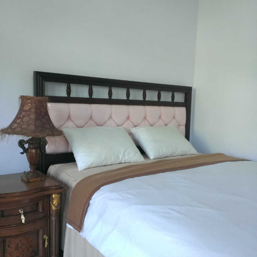 Headboard tempat tidur queen-size dengan bantal putih dan bed cover